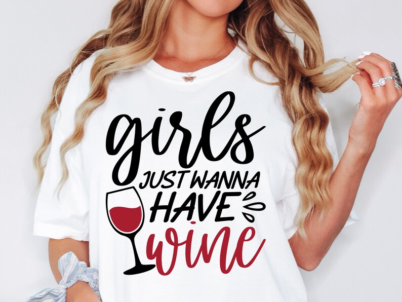 Puede incluir: Una camiseta blanca con texto en negro y rojo que dice "girls JUST WANNA HAVE wine" junto a un gr&aacute;fico de una copa de vino llena de l&iacute;quido rojo. El dise&ntilde;o est&aacute; centrado en la zona del pecho de la prenda y utiliza una mezcla de fuentes.