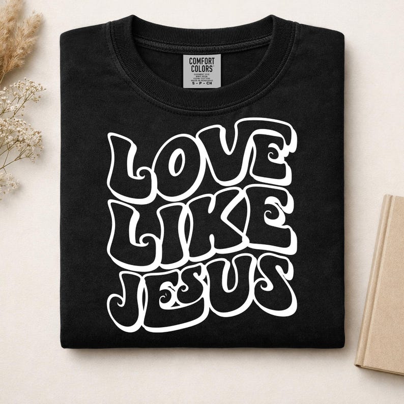 Pu&ograve; includere: Una t-shirt nera a girocollo con la scritta bianca LOVE LIKE JESUS in un carattere audace, ondulato e di ispirazione retr&ograve;. La maglietta presenta un'etichetta del marchio Comfort Colors stampata all'interno del colletto, indicante la taglia S.