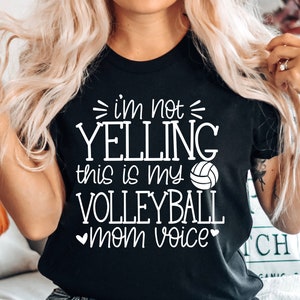 May include: Black t-shirt with white text that reads "I'm not yelling this is my volleyball mom voice" with a white volleyball graphic.
