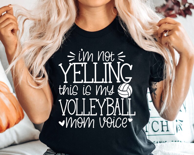 May include: Black t-shirt with white text that reads "I'm not yelling this is my volleyball mom voice" with a white volleyball graphic.