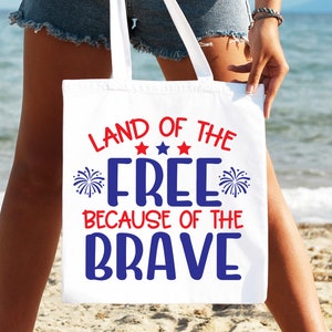 K&ouml;nnte beinhalten: Wei&szlig;e Einkaufstasche mit rot-wei&szlig;-blauem Text, der "Land of the Free Because of the Brave" lautet. Der Text ist von roten Sternen und blauen Feuerwerksmotiven umgeben.
