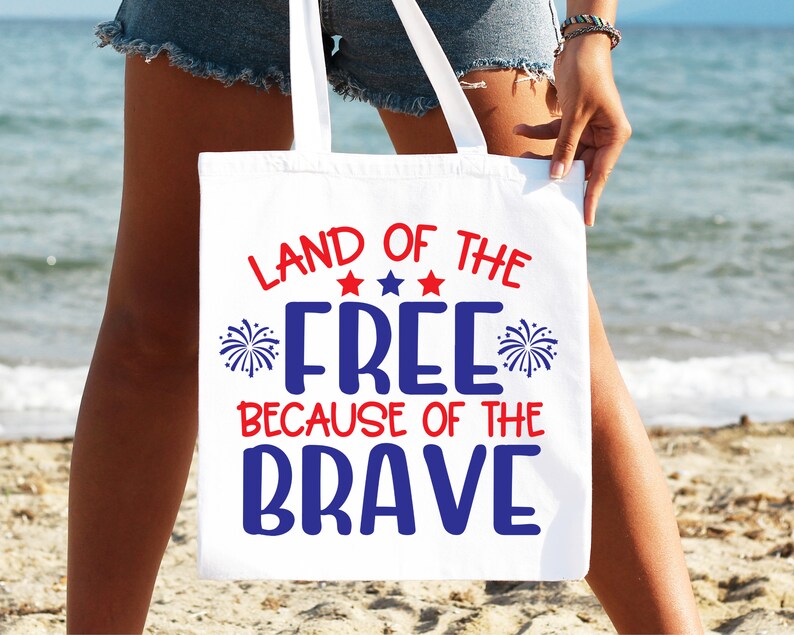 K&ouml;nnte beinhalten: Wei&szlig;e Einkaufstasche mit rot-wei&szlig;-blauem Text, der "Land of the Free Because of the Brave" lautet. Der Text ist von roten Sternen und blauen Feuerwerksmotiven umgeben.