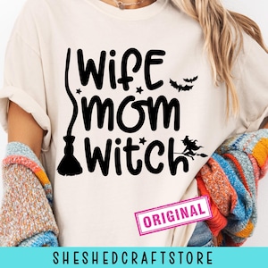 May include: A cream-colored t-shirt with the words "Wife Mom Witch" in black, along with a broom, stars, and bats. The shirt has a pink "ORIGINAL" stamp and the shop name "SHESHEDCRAFTSTORE" at the bottom.