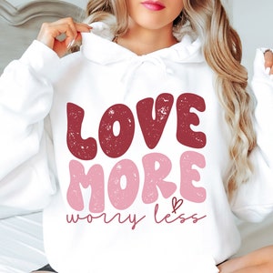 May include: White hoodie with a red and pink graphic that says "Love More Worry Less" in a distressed font.