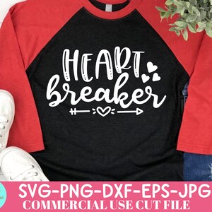 May include: A black and red raglan shirt with the words "Heartbreaker" in white script. The design includes hearts and an arrow. The shirt is paired with white sneakers and blue jeans.