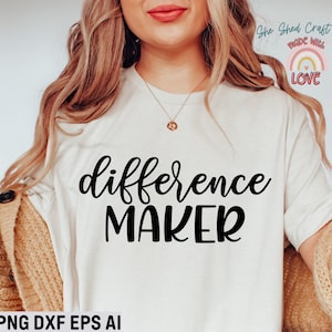 May include: A white t-shirt with the text "difference maker" in black cursive lettering. The shirt is being worn by a person with long blonde hair. The text "She Shed Craft Store Made With Love" is visible in the upper right corner of the image.
