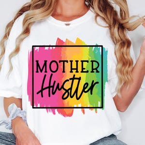 May include: White t-shirt with a rainbow paintbrush design and the text "Mother Hustler" in a black box.
