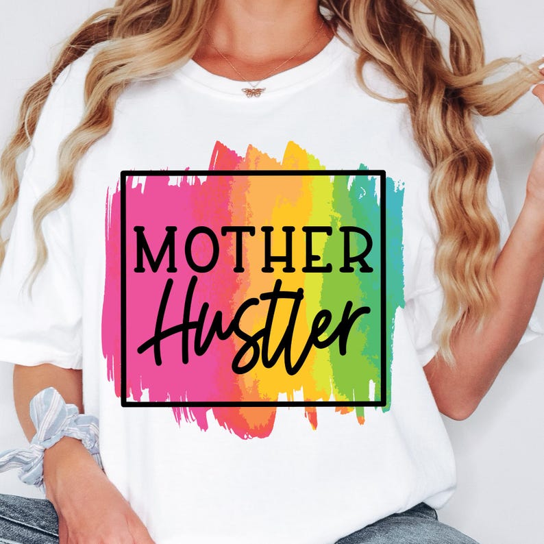May include: White t-shirt with a rainbow paintbrush design and the text "Mother Hustler" in a black box.