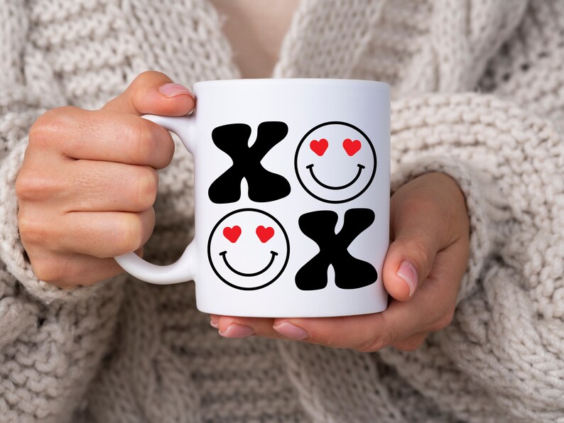 Pu&ograve; includere: Tazza in ceramica bianca con un design in bianco e nero che presenta le lettere "XO" e due facce sorridenti con cuori rossi come occhi.