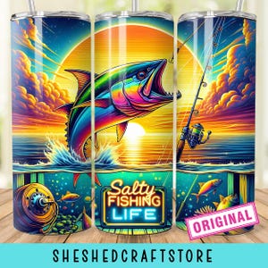 May include: A stainless steel travel mug with a colourful fishing scene. The design shows a fish jumping out of the water with a sunset in the background. Text includes "Salty Fishing Life" and "Original". The bottom text reads "SHESHEDCRAFTSTORE".