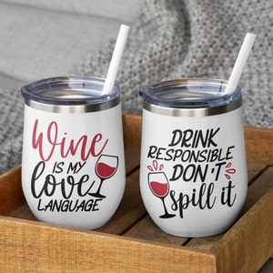 Puede incluir: Dos vasos blancos de acero inoxidable con tapas transparentes y pajitas blancas. El vaso izquierdo tiene texto en rojo y negro que dice Wine is my love language con un icono de copa de vino. El derecho tiene texto en negro y rojo que dice DRINK RESPONSIBLE DON'T spill it con un icono de copa de vino.