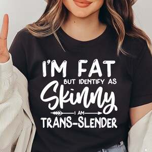 May include: Black t-shirt with white text that reads "I'm fat but identify as skinny - I am trans-slender".