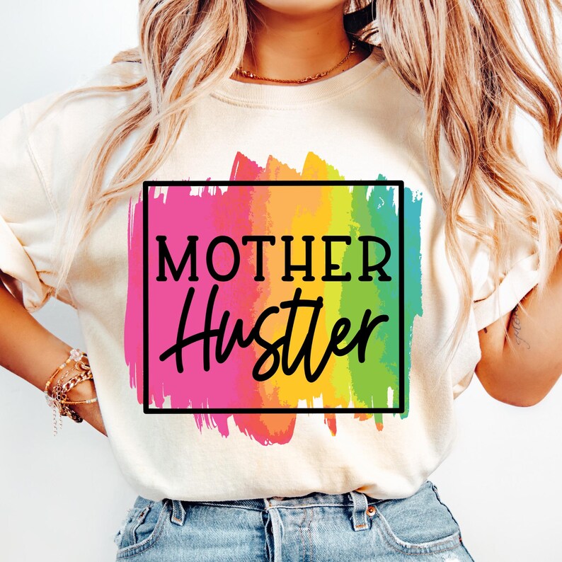 May include: A white t-shirt with a rainbow paintbrush design and the text "MOTHER Hustler" in a black square.