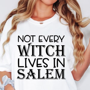 May include: White t-shirt with the black text "NOT EVERY WITCH LIVES IN SALEM." The shirt has a crew neck and short sleeves. The text is in a bold, stylized font. The shirt is a casual, everyday wear item.