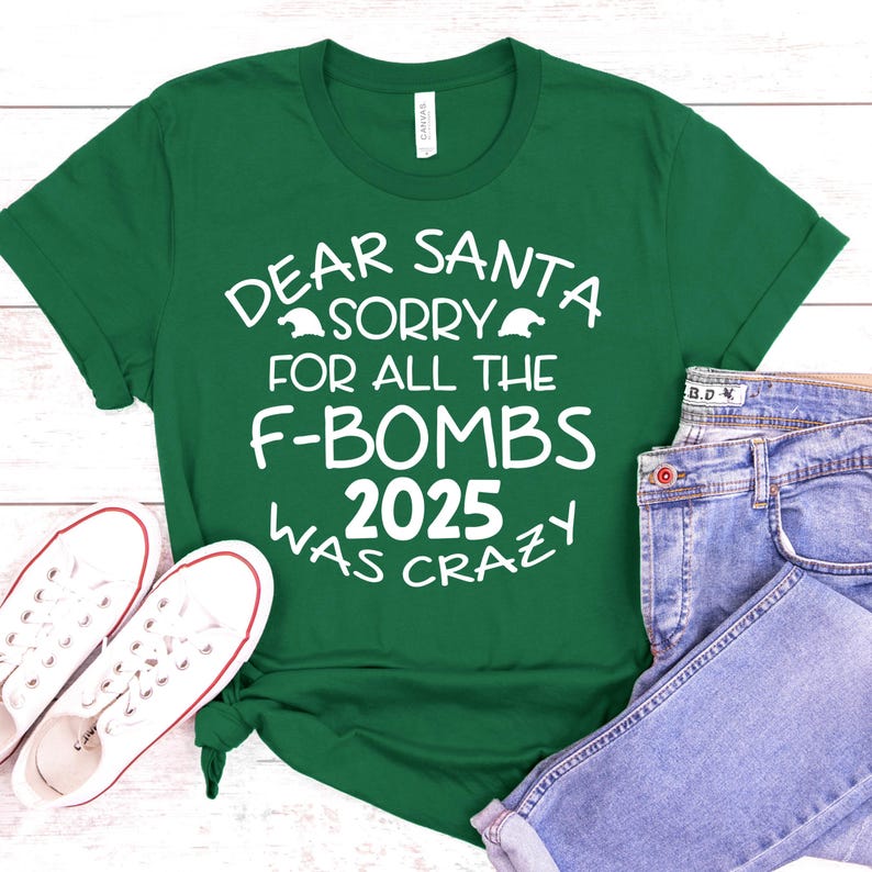 May include: A green t-shirt with the text "DEAR SANTA SORRY FOR ALL THE F-BOMBS 2025 WAS CRAZY" in white. The shirt is paired with blue jeans and white sneakers.