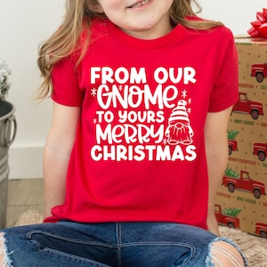 May include: Red t-shirt with white text that says "From our *Gnome* to yours *Merry* Christmas" and a white cartoon gnome wearing a red hat.