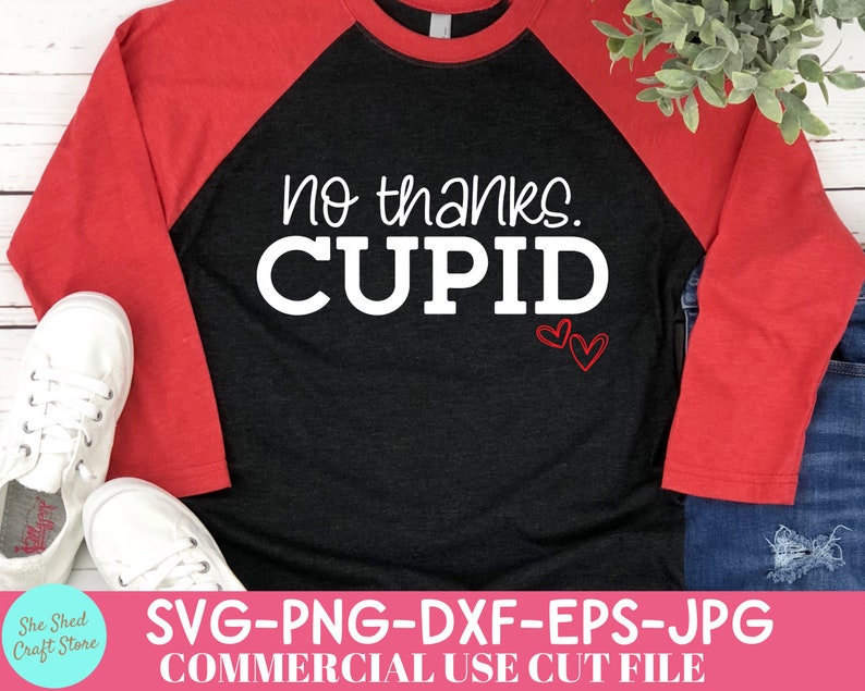 May include: A black and red raglan shirt with the text "no thanks. CUPID" in white. Two red heart outlines are below the text. The shirt is paired with blue jeans and white sneakers.