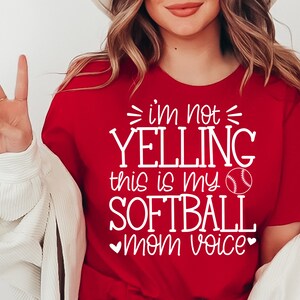 May include: Red t-shirt with white text that reads "I'm not yelling this is my softball mom voice" with a white baseball graphic.