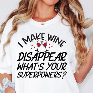 Puede incluir: Una camiseta blanca de manga corta con el texto en negro "I MAKE WINE DISAPPEAR WHAT'S YOUR SUPERPOWERS?" y un gr&aacute;fico de dos copas de vino tinto brindando, acentuado por peque&ntilde;as formas de estrellas rojas situadas sobre el texto.