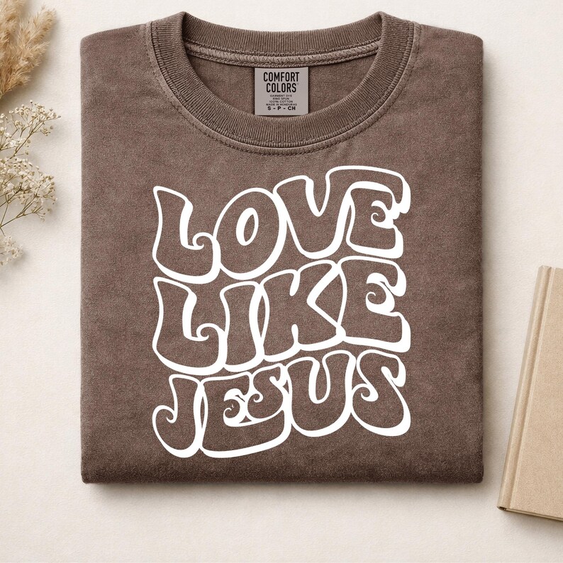 Pu&ograve; includere: Una t-shirt marrone a girocollo con il testo bianco LOVE LIKE JESUS in un carattere audace, ondulato e di ispirazione retr&ograve;. La maglietta presenta un'etichetta del marchio Comfort Colors sul colletto interno, che indica la taglia S-P-CH.