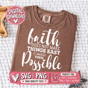 Può includere: Una t-shirt marrone a maniche corte con testo bianco che recita: faith DOES NOT MAKE THINGS EASY IT MAKES THEM POSSIBLE. La maglia presenta un girocollo e un'etichetta del marchio Comfort Colors sul colletto interno. È presente un grafico per il download digitale.