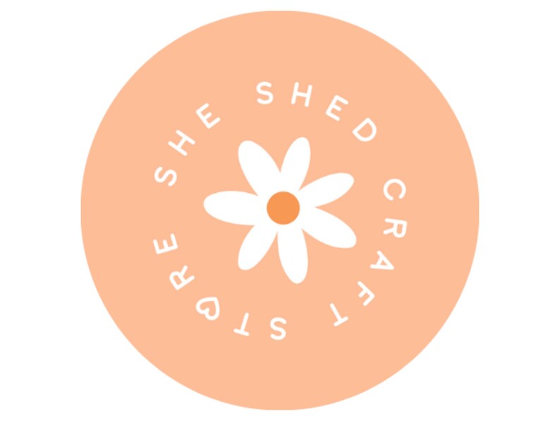 K&ouml;nnte beinhalten: Ein pfirsichfarbener Kreis mit dem Text "She Shed Crafts" in wei&szlig;en Buchstaben um eine wei&szlig;e Margerite mit gelber Mitte.