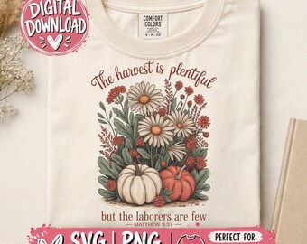 May include: A cream-colored t-shirt featuring a graphic of white and orange pumpkins surrounded by daisies and wildflowers. The text reads, The harvest is plentiful but the laborers are few, with the reference Matthew 9:37 printed below.
