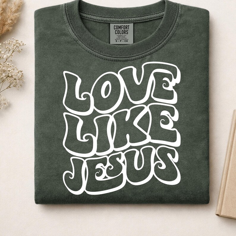 Pu&ograve; includere: Una t-shirt a girocollo verde oliva scuro con la scritta bianca LOVE LIKE JESUS in un carattere audace, ondulato e di ispirazione retr&ograve;. La maglietta presenta un'etichetta del marchio Comfort Colors all'interno del collo, indicante la taglia S.