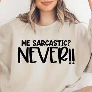 May include: A light beige sweatshirt with the text "ME SARCASTIC? NEVER!" printed in black.