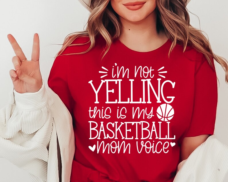May include: Red t-shirt with white text that reads "I'm not yelling this is my basketball mom voice" and a white basketball graphic.