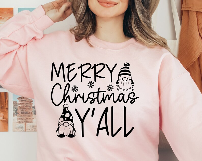 May include: A pink sweatshirt with the text "Merry Christmas Y'all" in black lettering. Two gnomes are featured on the sweatshirt, one with a black and white striped hat and the other with a black and white polka dot hat.