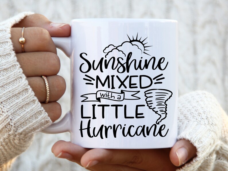 May include: White ceramic mug with the text "Sunshine Mixed with a Little Hurricane" in black script. The design includes a sun, clouds, and a tornado illustration. The mug has a curved handle.