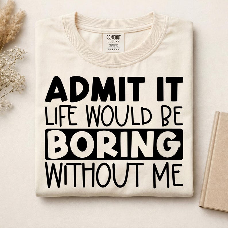 May include: A cream-colored crew neck t-shirt with black text that reads ADMIT IT LIFE WOULD BE BORING WITHOUT ME. The shirt features a Comfort Colors brand label at the inner neckline and is folded neatly on a flat surface.