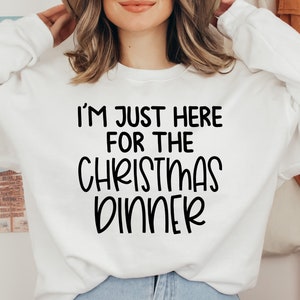 Peut inclure: Sweat-shirt blanc avec un texte noir qui dit "Je suis juste l&agrave; pour le d&icirc;ner de No&euml;l."