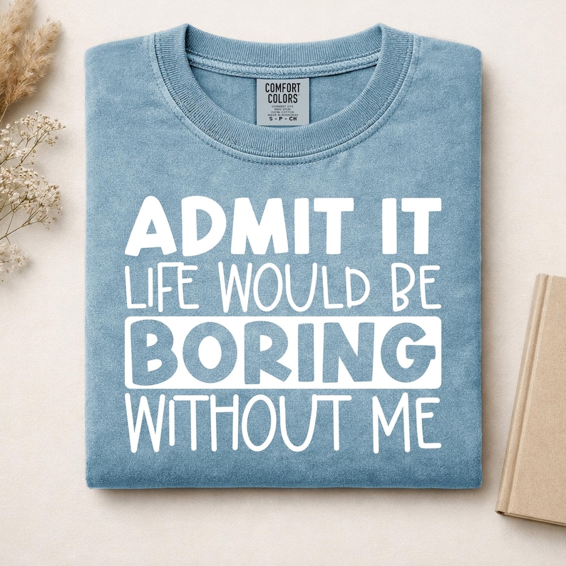 May include: A blue crew neck t-shirt with white text that reads: ADMIT IT LIFE WOULD BE BORING WITHOUT ME. The shirt features a Comfort Colors brand label at the inner neckline and has a soft, washed-out appearance.