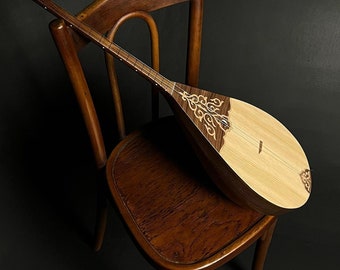 May include: A traditional stringed musical instrument, possibly a lute, is displayed on a vintage wooden chair. The instrument has a light-toned soundboard and a dark, decorative wooden body with inlays. The chair has a curved back and a warm, brown finish.
