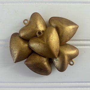 May include: A cluster of six gold-colored metal heart-shaped charms. The charms are arranged in a circular pattern, with the points of the hearts facing outward.