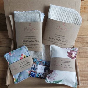 May include: A box filled with eco-friendly cleaning products. The products include a cotton waffle cloth, a linen cleaning cloth, a floral patterned sponge scrubber, and a floral patterned sponge. The products are handmade in Wirral, UK. The box is labeled "Mary Makes Zero Waste".