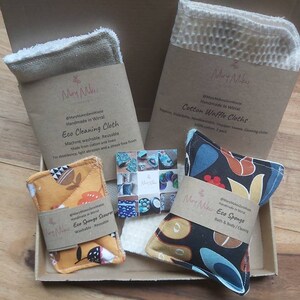 May include: A gift box filled with eco-friendly cleaning and bath products. The box contains a brown and white cotton waffle cloth, a brown and white eco cleaning cloth, a yellow and orange eco sponge scourer, and a black and blue eco sponge. The products are handmade in Wirral.