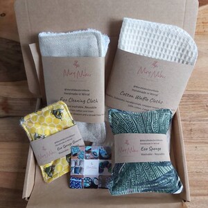 May include: A cardboard box filled with eco-friendly cleaning supplies. The box contains a set of cotton waffle cloths, a linen cleaning cloth, a yellow sponge with a bee design, and a green sponge with a leafy pattern. The products are labeled "Mary Makes Zero Waste" and "Handmade in Wirral".