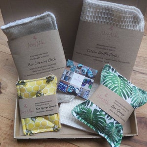 May include: A gift box filled with eco-friendly cleaning and bath products. The box contains a cotton waffle cloth, a reusable cleaning cloth, a sponge scrubber, and a bath sponge. The products are all handmade in Wirral and feature a variety of designs.