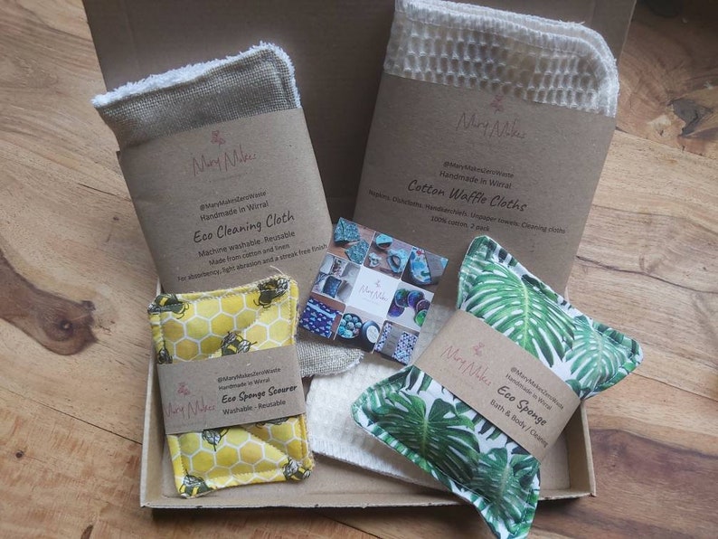 May include: A gift box filled with eco-friendly cleaning and bath products. The box contains a cotton waffle cloth, a reusable cleaning cloth, a sponge scrubber, and a bath sponge. The products are all handmade in Wirral and feature a variety of designs.