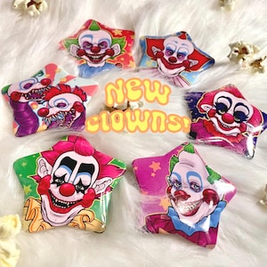 May include: Five star-shaped pins featuring colorful clown illustrations with red noses, painted faces, and varied expressions. The text "NEW CLOWNS!" is centered in yellow bubble letters. Each pin displays a unique clown character with vibrant hair.