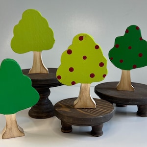 May include: Four wooden trees painted in green and yellow with red polka dots. The trees are on small wooden stands with three legs.