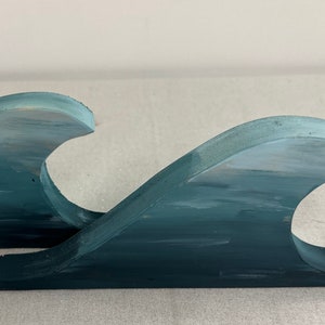 Peut inclure: Deux sculptures d'ondes en bois peintes dans des tons de bleu et de blanc. Les vagues sont empilées l'une sur l'autre, créant un effet de superposition.