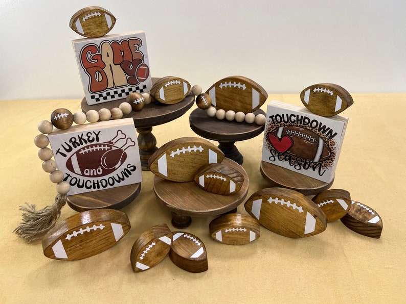 May include: Wooden signs with football themes, including "Game Day", "Turkey and Touchdowns", and "Touchdown Season". The signs are decorated with painted footballs and other festive details.