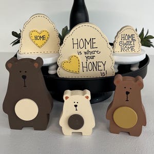 May include: Wooden bear figurines in shades of brown and cream, with a yellow circle accent. Decorative signs with the phrases "Home Sweet Home" and "Home is where your honey is!" are also present.
