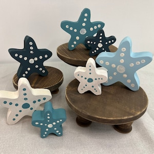 May include: A tiered wooden stand with four painted wooden starfish. The starfish are painted in shades of blue and white with white dots. The stand is a dark brown color.