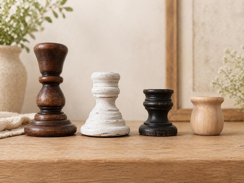 Peut inclure: Quatre bougeoirs en bois de diff&eacute;rentes formes et couleurs. Le plus grand est brun fonc&eacute;, suivi d'un blanc vieilli, d'un noir et d'un support en bois naturel. Ils sont dispos&eacute;s sur une surface en bois.