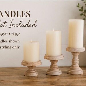 May include: Three cream-colored pillar candles on decorative wooden candle holders. The candle holders have a distressed, carved design. The text in the image reads "CANDLES Not Included" and "Candles shown for styling only."